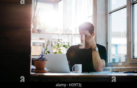 Shot of serious young man finding ideas while working on laptop. Male entrepreneur sitting at his desk and looking at laptop com Stock Photo