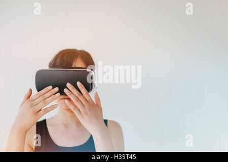 Shot of young woman wearing virtual reality goggle against grey background. Female with VR headset connecting device making gest Stock Photo