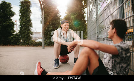 Young friends sitting on basketball court. Streetball players taking rest after playing a game. Two young men relaxing and takin