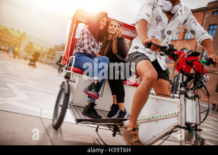 Shot of teenage girls taking selfie on tricycle ride. Young female friends riding on tricycle bike and taking self portrait. Stock Photo