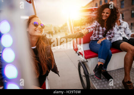 Best friends enjoying tricycle ride in the city. Teenage girls riding on tricycles and holding hands. Stock Photo