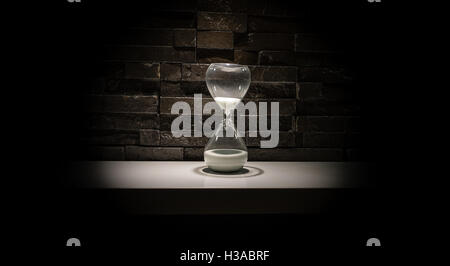 Broken hourglass, sand clock on a dark gray brick wall background Stock Photo