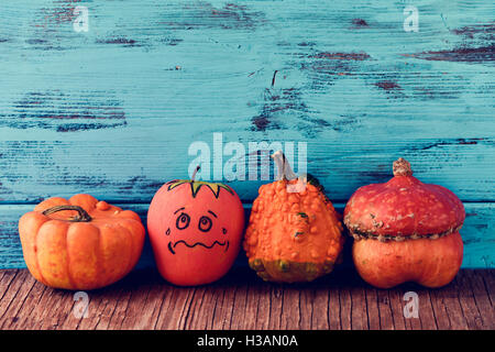 an apple disguised as a pumpkin with a funny face trying to go unnoticed between different real pumpkins, on a rustic wooden sur Stock Photo