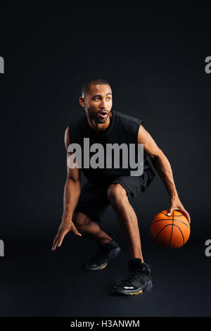 Portrait of a focused young african sports man playing in basketball isolated on a black background Stock Photo