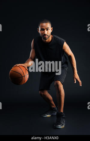 Portrait of a serious african sports man playing in basketball isolated on a black background Stock Photo