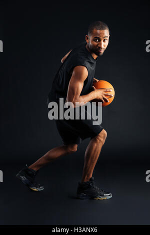 Portrait of a focused young african sports man playing in basketball isolated on a black background Stock Photo