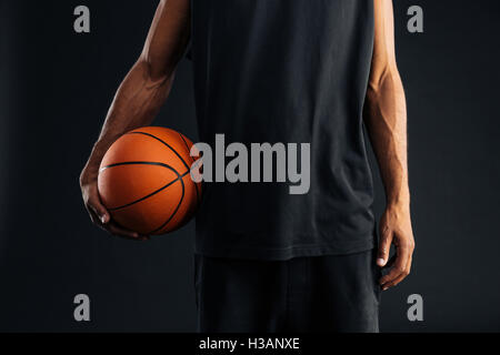 Cropped image of an african basketball player holding ball isolated on a black background Stock Photo