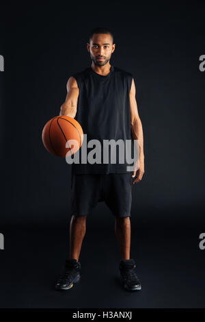 Focused young african basketball player giving ball isolated on a black background Stock Photo