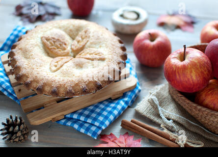 Apple pie with fruit ingredients autumn leaves and cinammon sticks on a wooden table