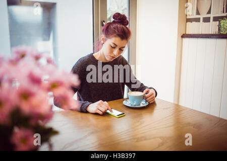 Hipster drinking a cup of coffee while using a smartphone Stock Photo