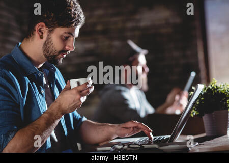 Side view of man drinking coffee while working on laptop Stock Photo