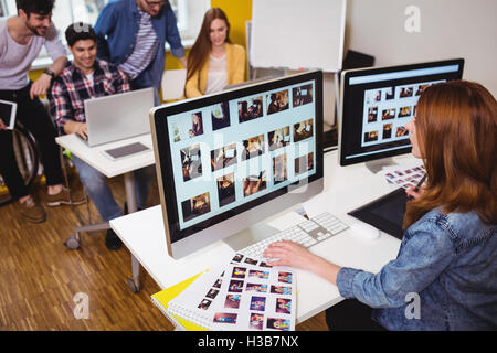 Female photo editor working on computer against coworkers Stock Photo