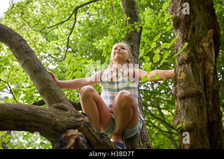 happy girl climbing up tree in summer park Stock Photo