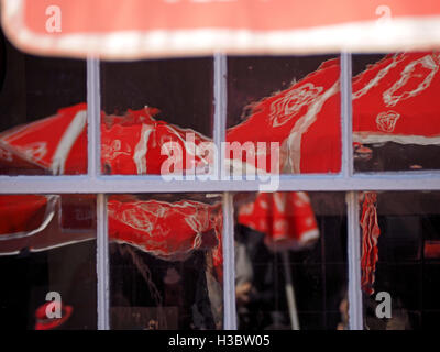 reflection of red advertising umbrellas and red hat in glass of white painted panelled sash window Stock Photo