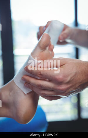 Male therapist putting bandage on female patient foot Stock Photo