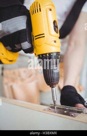 Carpenter tightening screw to hinges on a wooden door Stock Photo