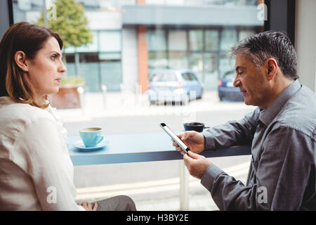 Man using mobile phone while talking with woman Stock Photo