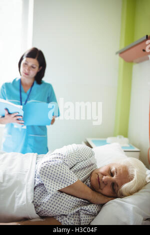 Senior patient sleeping on a bed while nurse checking report Stock Photo