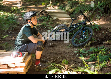 Thoughtful male cyclist sitting in forest Stock Photo