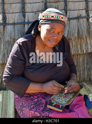 Zulu woman troupe member in traditional clothes making bead souvenirs in front a Zulu rondavel ,Shakaland Cultural Village,KwaZulu-Natal,South Africa