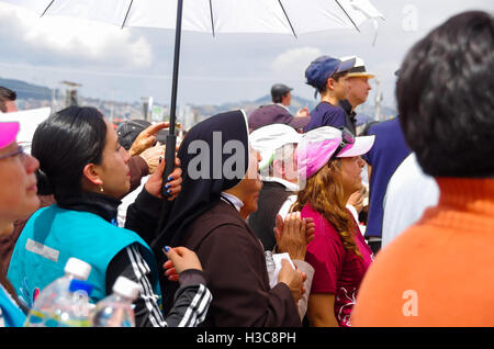 QUITO, ECUADOR - JULY 7, 2015: In the middle of thousand people a nun is praying under the sun, a police is behind her Stock Photo