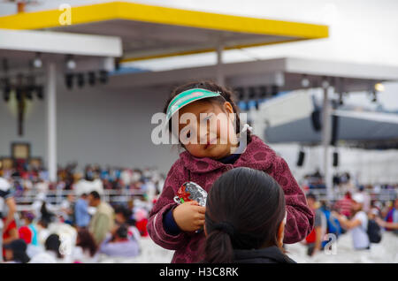 QUITO, ECUADOR - JULY 7, 2015: Confused face of a girl with a little hat waitting in the mass of pope Francisco event, chips in her hands Stock Photo