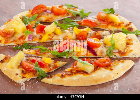 Stone baked thin crust pizza with pineapple, pepper and red onions sprinkled with sea salt and rocket leaves Stock Photo