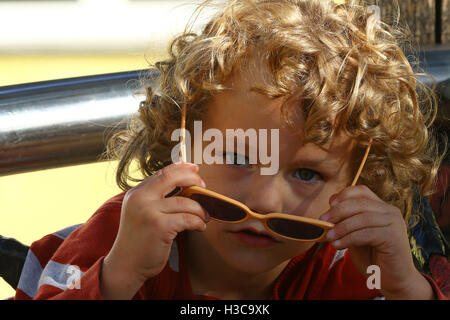 Blonde curly haired child with sunglasses playing at the playground Stock Photo