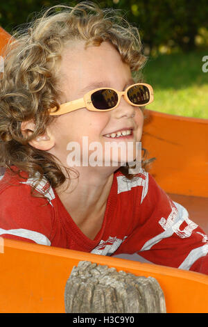 Blonde curly haired child with sunglasses playing at the playground Stock Photo