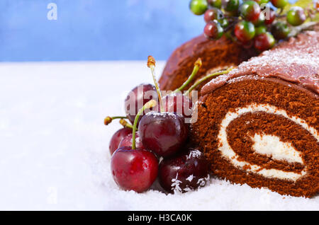 Christmas Yule Log, Buche de Noel, chocolate cake with branch, fresh cherries and festive berry decorations on a white serving p Stock Photo