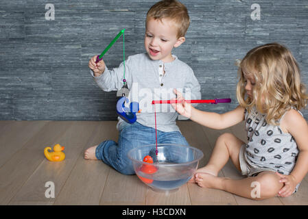 Children using toy fishing rods to catch rubber ducks floating in large bowl Stock Photo