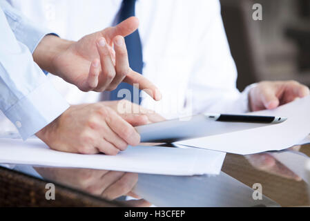 Businessman showing colleague how to use digital tablet Stock Photo