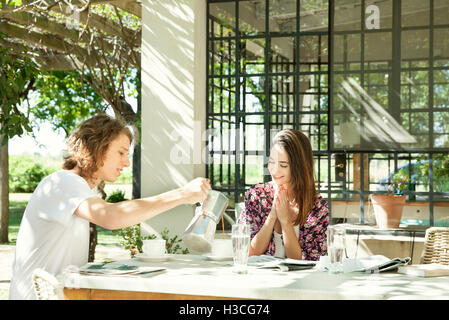 Young man pouring coffee for girlfriend at breakfast table outdoors Stock Photo