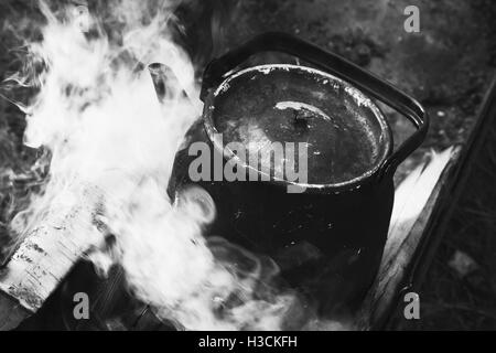 Old used teapot with boiling water stands on a bonfire, black and white photo Stock Photo