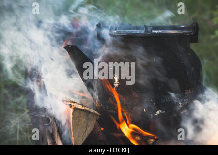 Old black teapot with boiling water stands on a bonfire Stock Photo