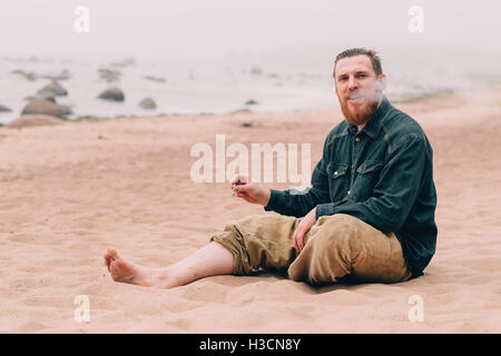 Serious bearded man smoking a cigarette on the beach Stock Photo