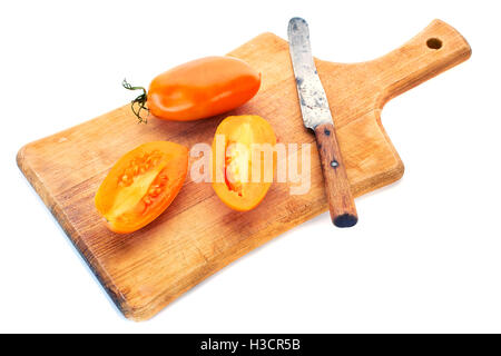 Yellow tomatoe with half slices and old knife on wooden board. Stock Photo