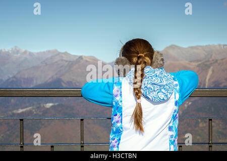 Girl with a pigtail, dressed in sports jacket and warm fluffy headphones, admires of autumn mountain landscape, Sochi, Russia Stock Photo