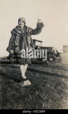Antique c1930 photograph, woman in fur coat balances on rock near a Ford automobile. Location: Massachusetts, New England, USA. SOURCE: ORIGINAL PHOTOGRAPHIC PRINT. Stock Photo