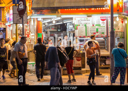 People in front of a street food stall at corner of Prat Ave and Hart Ave in Tsim Sha Tsui, Kowloon, Hong Kong, China at night. Stock Photo