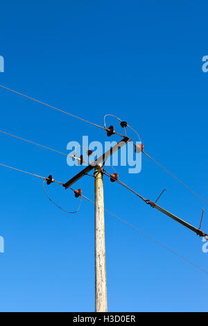 Detail of a wooden telegraph pole and wires with ceramic insulators on a clear blue sky background. Stock Photo