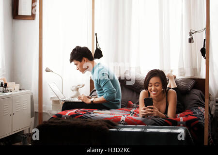 Happy couple using laptop and smart phone in bedroom Stock Photo