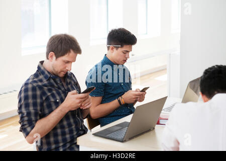 businessmen using smart phones at desk in creative office Stock Photo