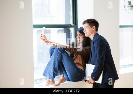 Happy business colleagues taking selfie through smart phone by window in creative office Stock Photo