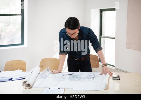 businessman analyzing blueprint at desk in creative office Stock Photo