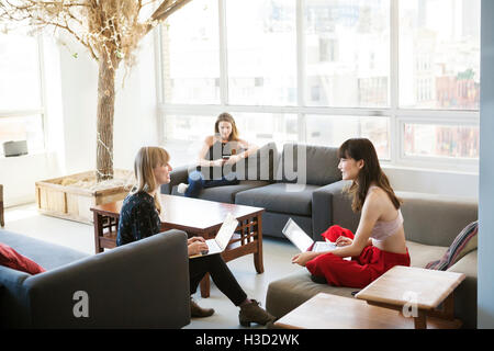 businesswomen discussing while colleague using phone in background Stock Photo