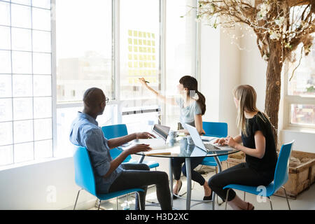 businesswoman writing on adhesive notes while discussing with colleagues Stock Photo