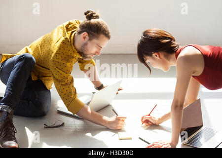 business people writing in notes on floor at brightly lit creative office Stock Photo