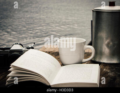 Close-up of open novel by coffee cup and camera on sidewalk cafe Stock Photo