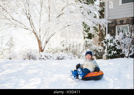 Happy girl sitting on inflatable ring in backyard during winter Stock Photo